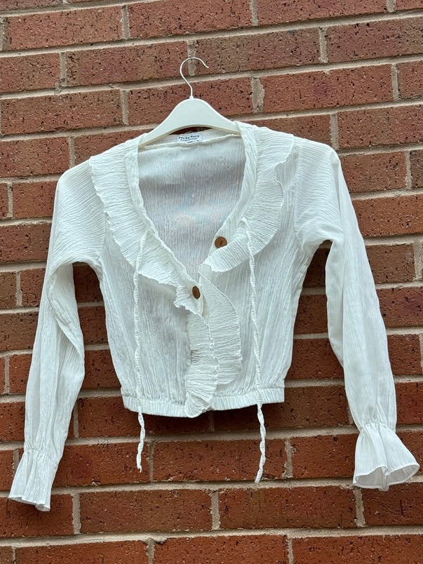 White Per Ka Nong top on a hanger against a brick wall