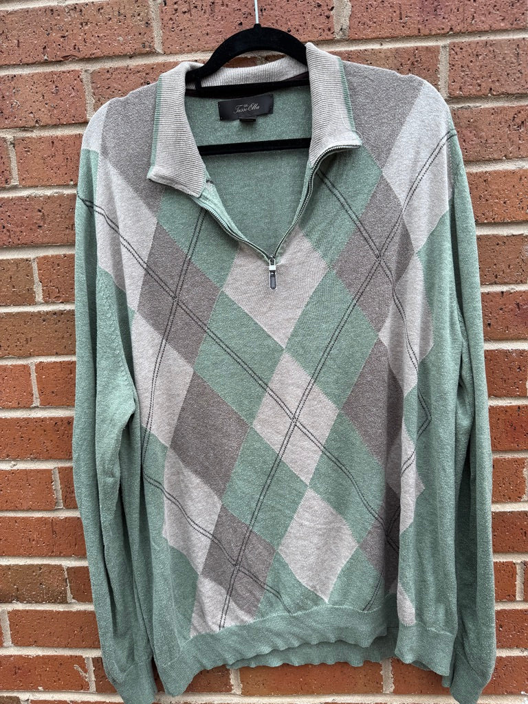 Green and gray argyle patterned sweater on a hanger against a brick wall.