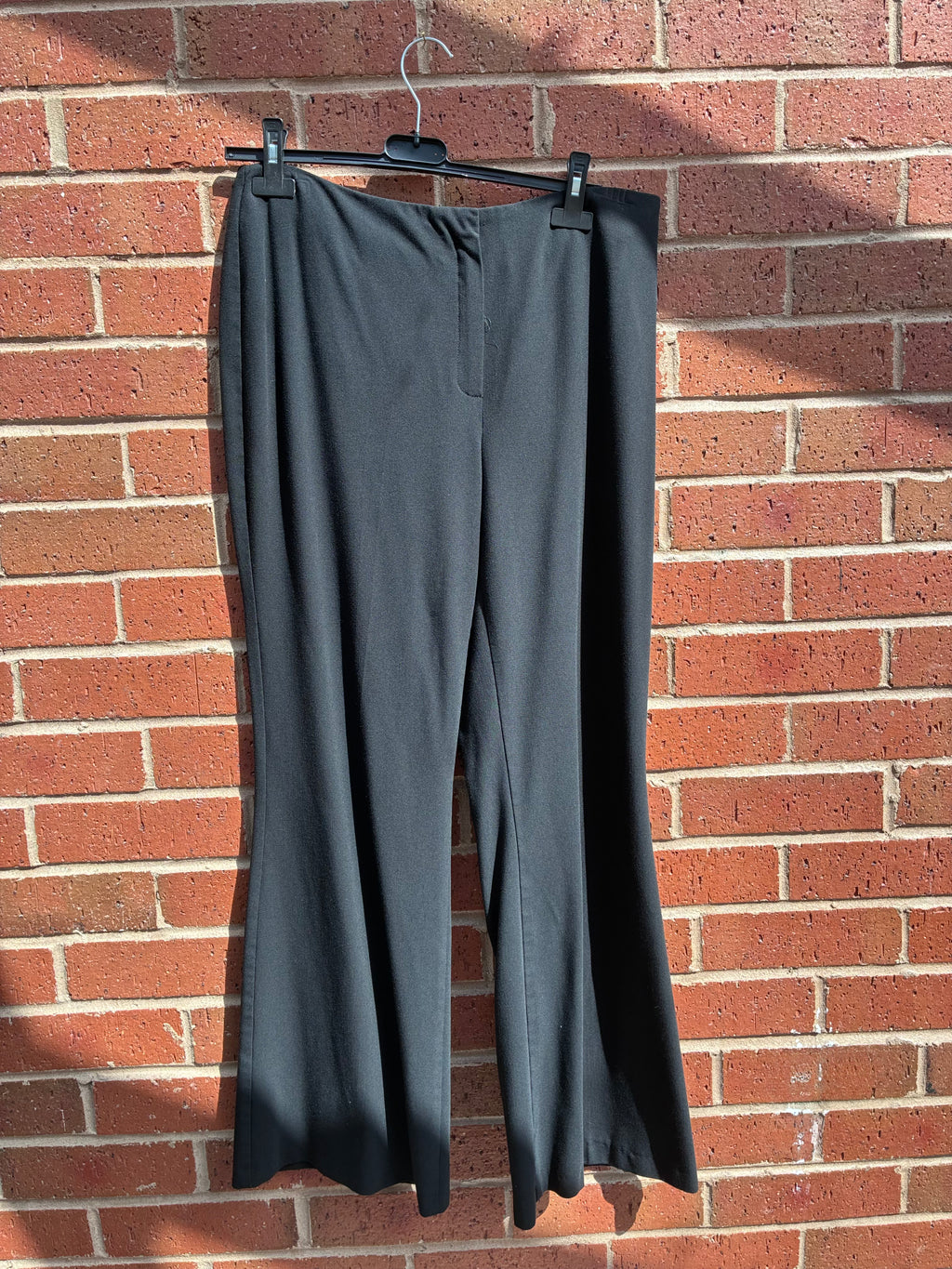 Black M&S womens trousers size 16 hanging on a hanger against a brick wall