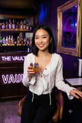 Woman holding a colourful drink in a bar with a Per Ka Nong crop-top on in white