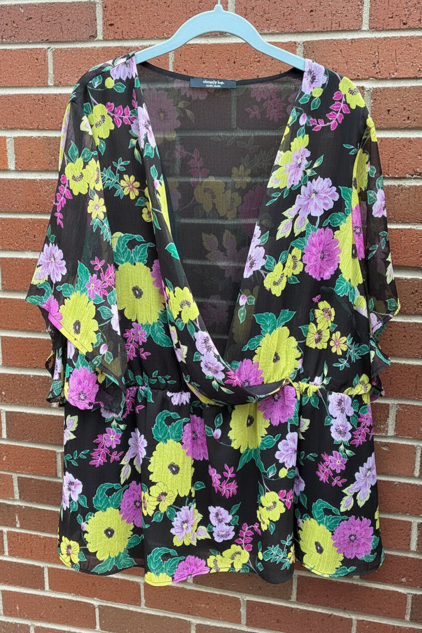 Floral-patterned wrap-front and peplum style blouse hanging against a brick wall